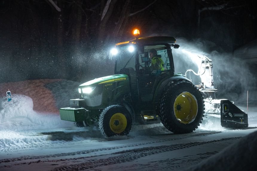 Tractor-mounted snow blower clearing a long driveway