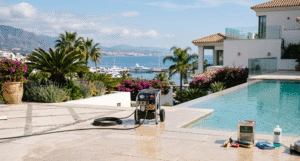 Professional crew executing deep cleaning and oleophobic sealing on a luxury travertine pool terrace in Marbella, overlooking Puerto Banús and the Mediterranean coast.